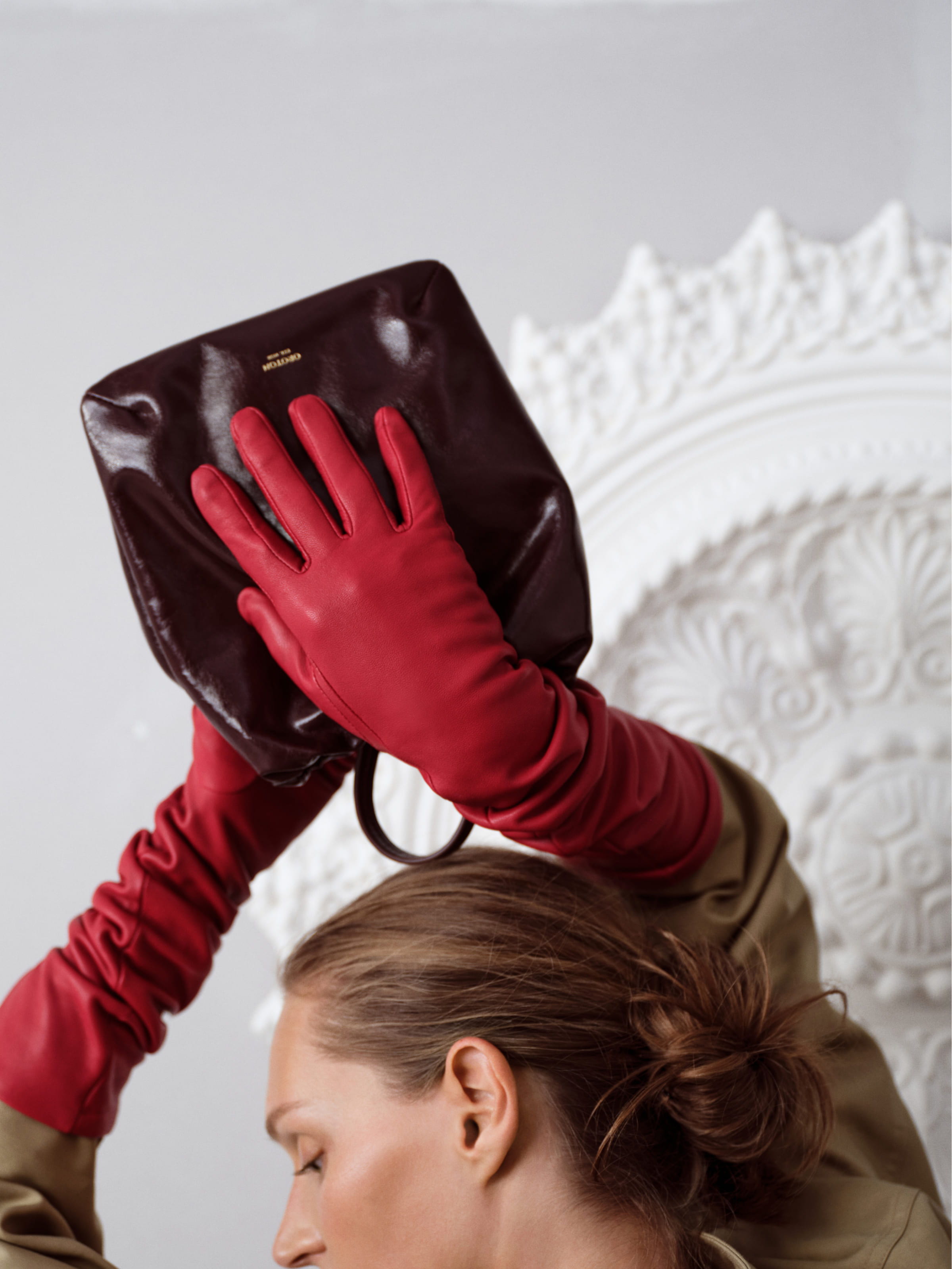 A person wearing red gloves holds a handbag against a decorative background.
