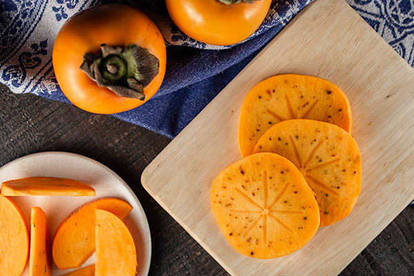 Sliced persimmons on a wooden board with whole fruits nearby.