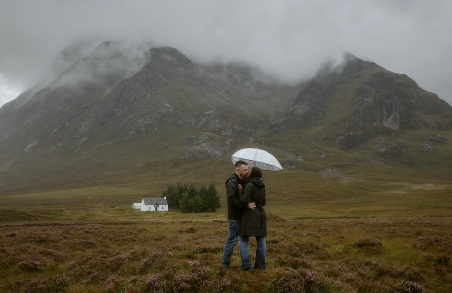 engaged couple kissing under umbrella in scottish highlands
