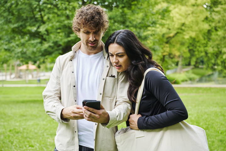 Two people looking at a smartphone together in a park.