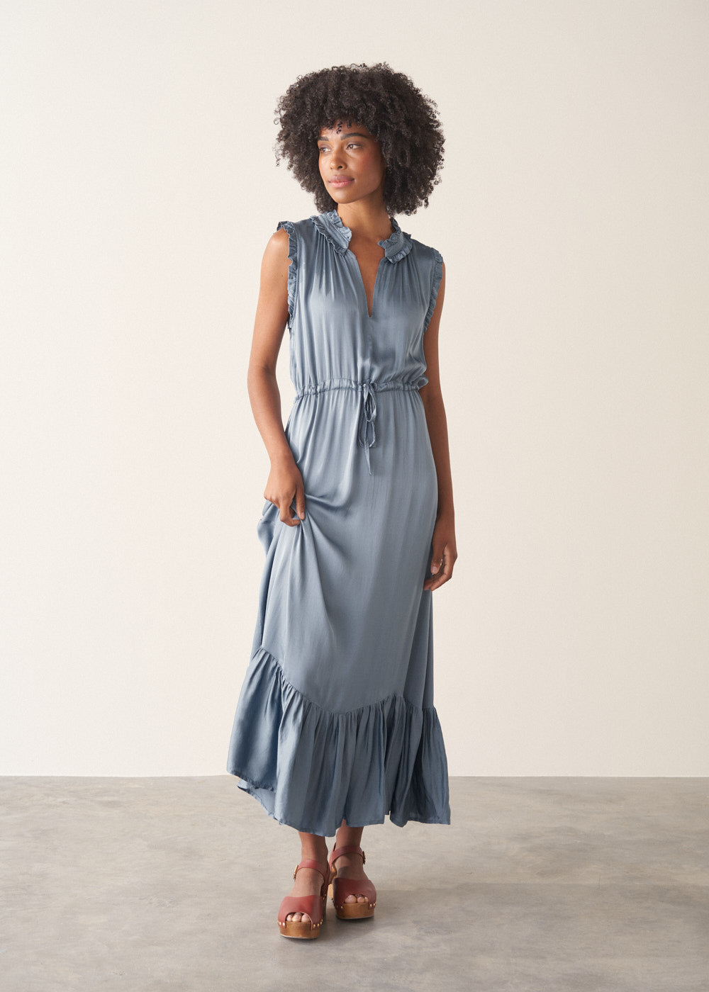 Woman wearing a dusky blue satin midi dress standing against a plain background
