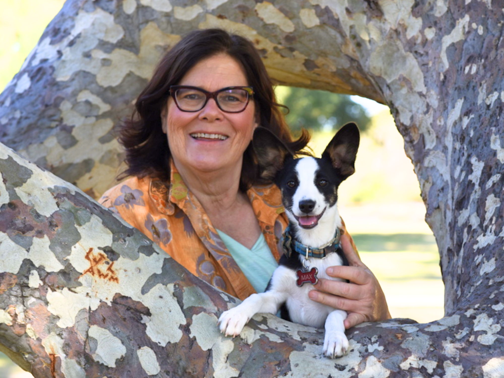 Dr. Dody smiling outdoors while holding her black and white puppy Max between the branches of a tree.