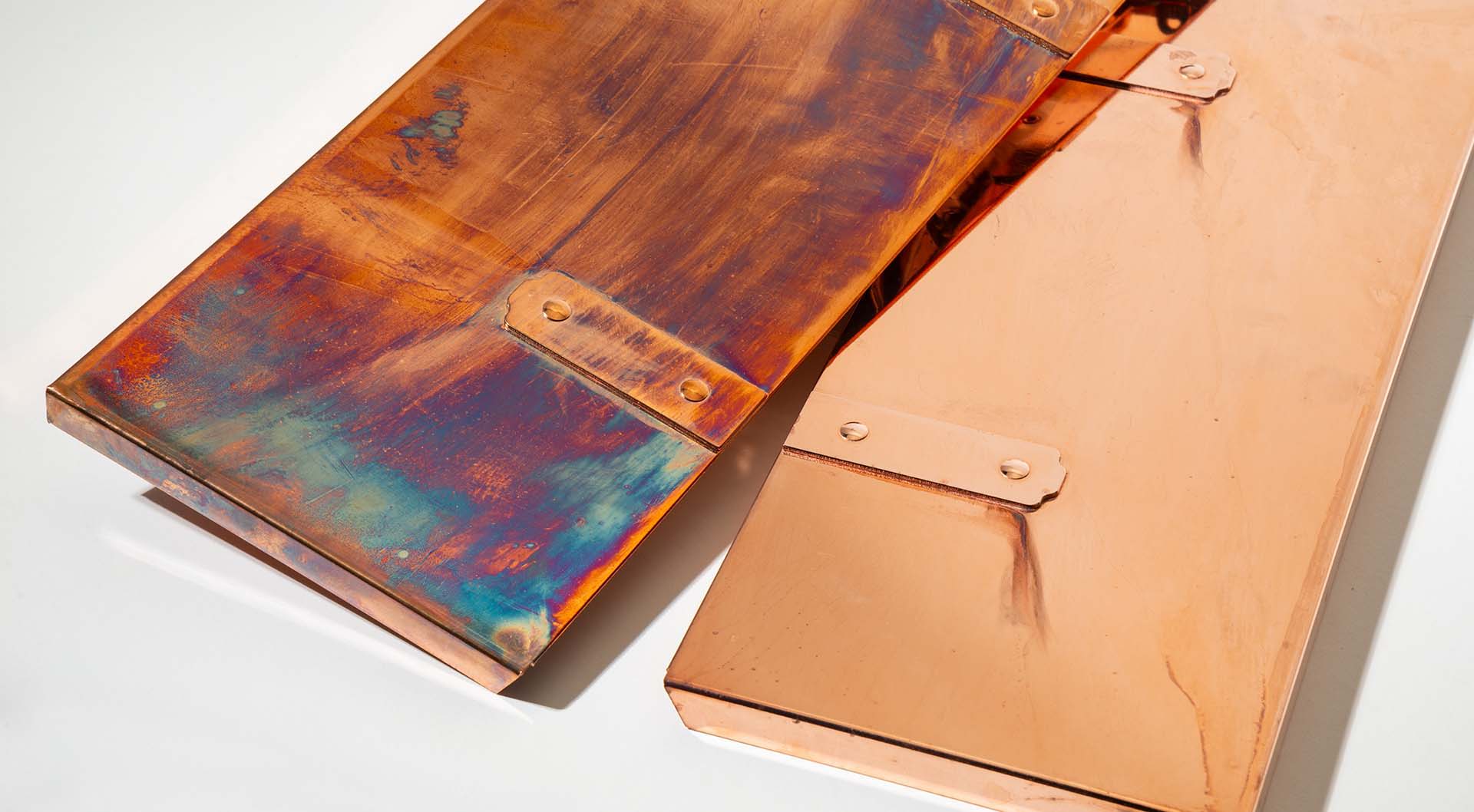 A pair of wall mount mailbox roofs with raw copper plating. One is relatively streak free and the other is covered in iridescent oxidization.