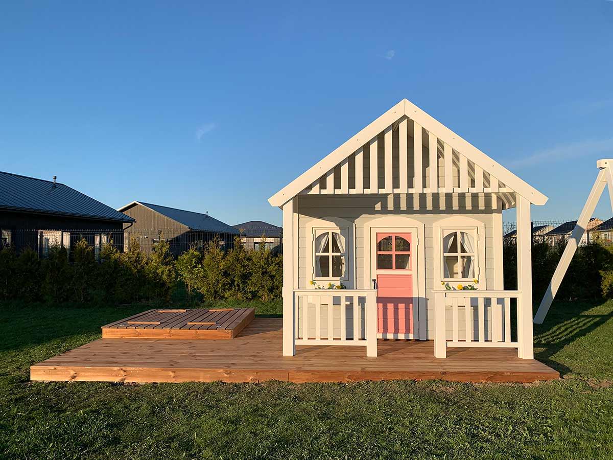 Front View Of  light Gray Custom Kids Playhouse With Pink Door And Wooden Terrace with Sandbox by WholeWoodPlayhouses 