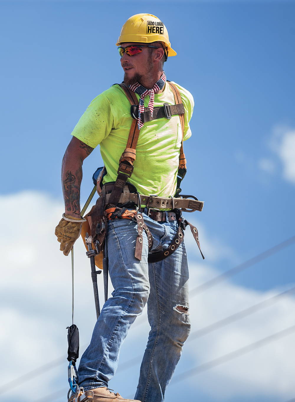 Construction worker wearing hi-vis shirt, safety glasses, fall protection harness and cap style hard hat with company logo custom printed on the side.