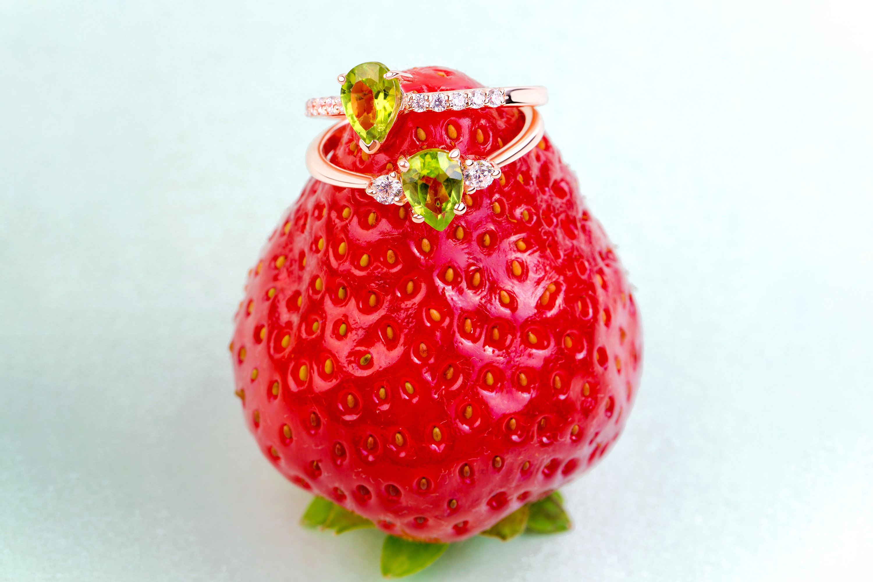 Two rings with Peridot gemstones are placed on a red strawberry.