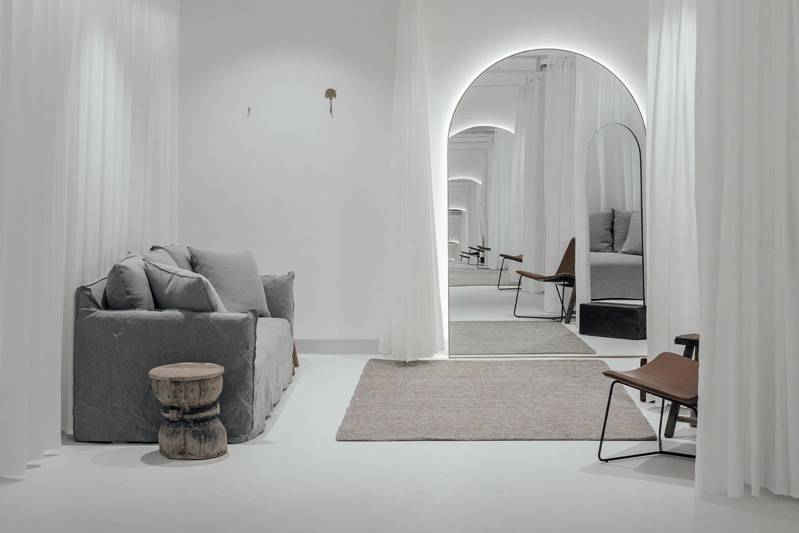 Modern interior with gray sofa, mirror, and minimalist decor in soft lighting.