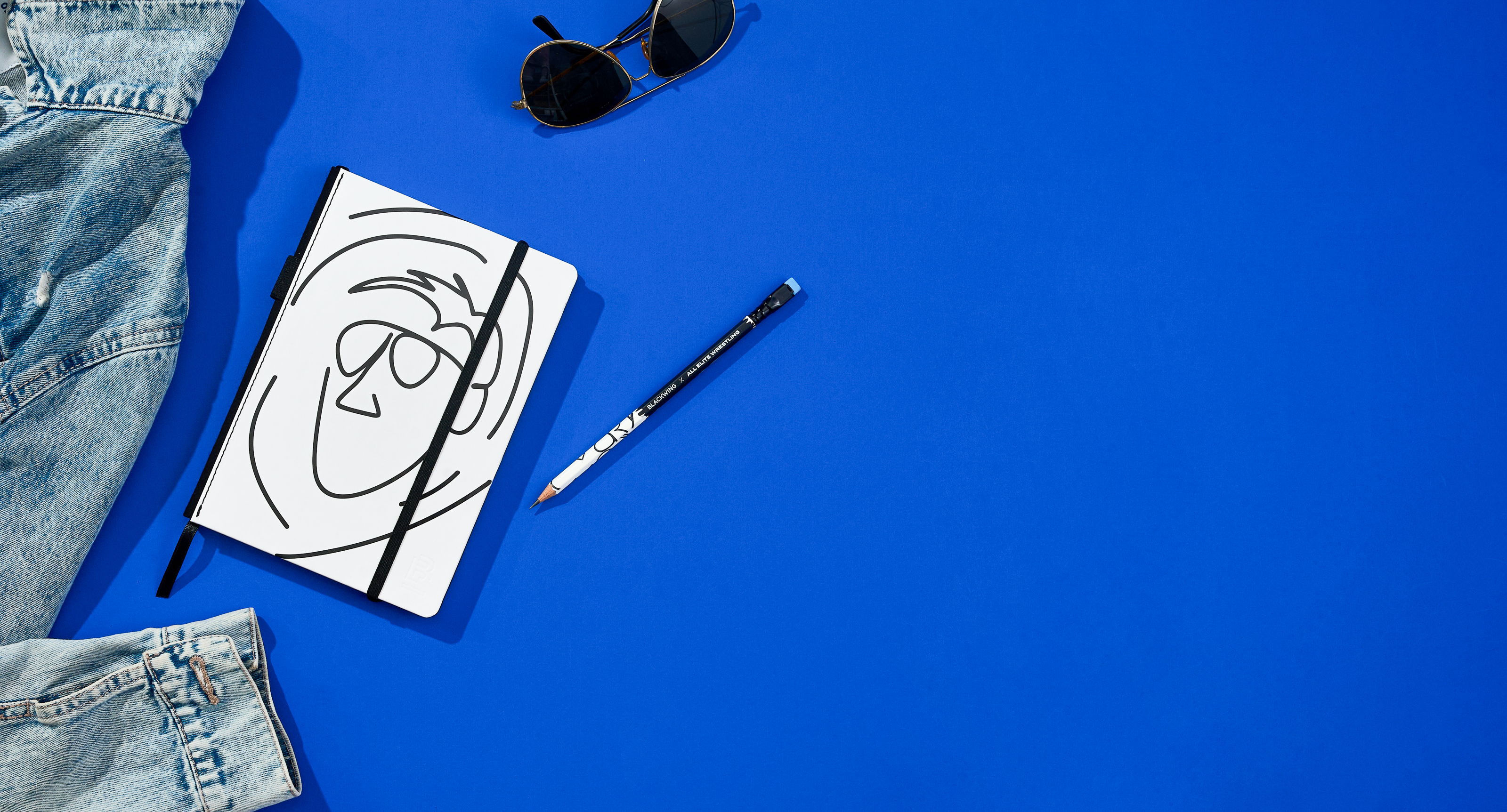 Notebook, sunglasses, pen, and denim on a bright blue background.