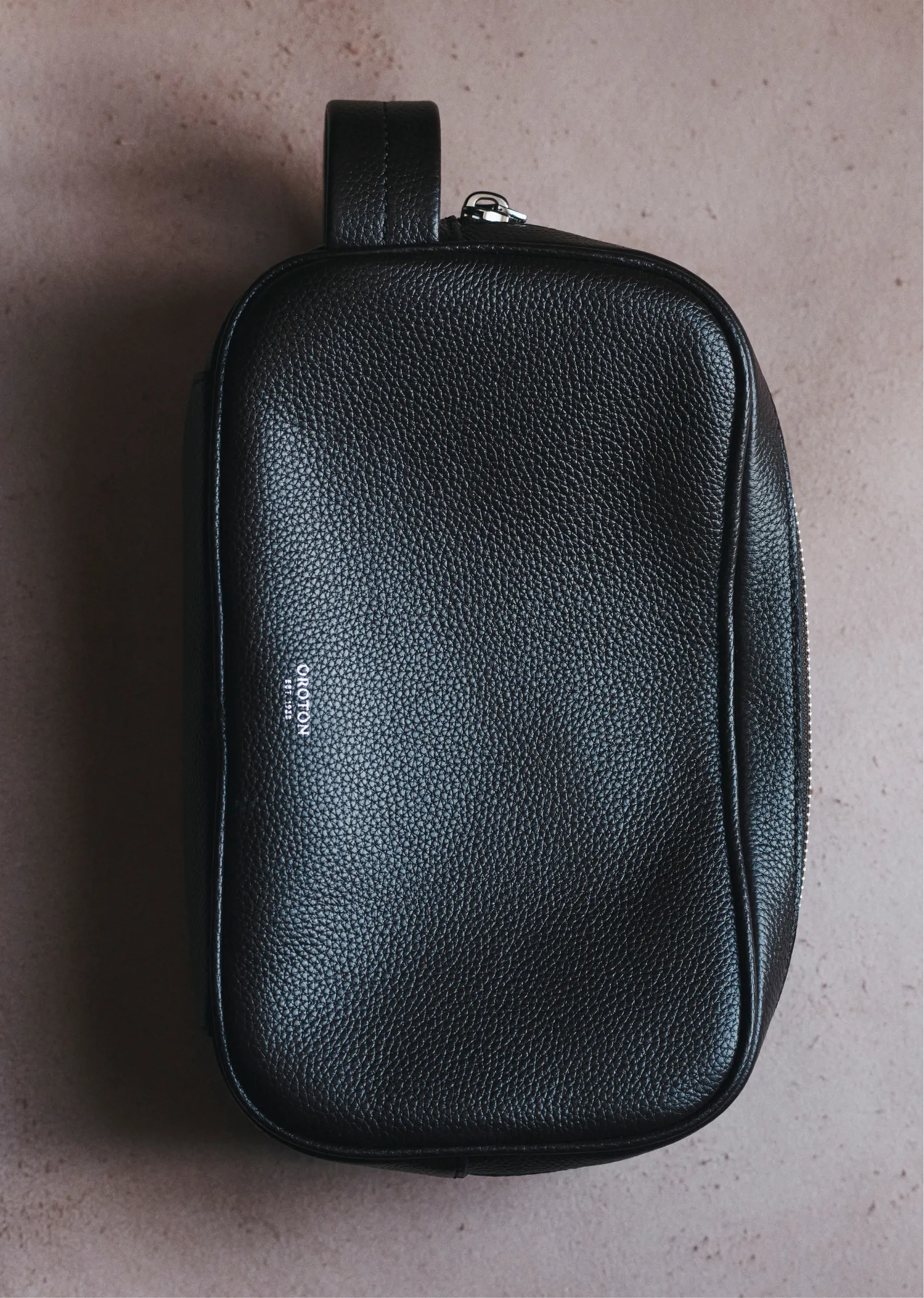 Black leather toiletry bag on a neutral surface.
