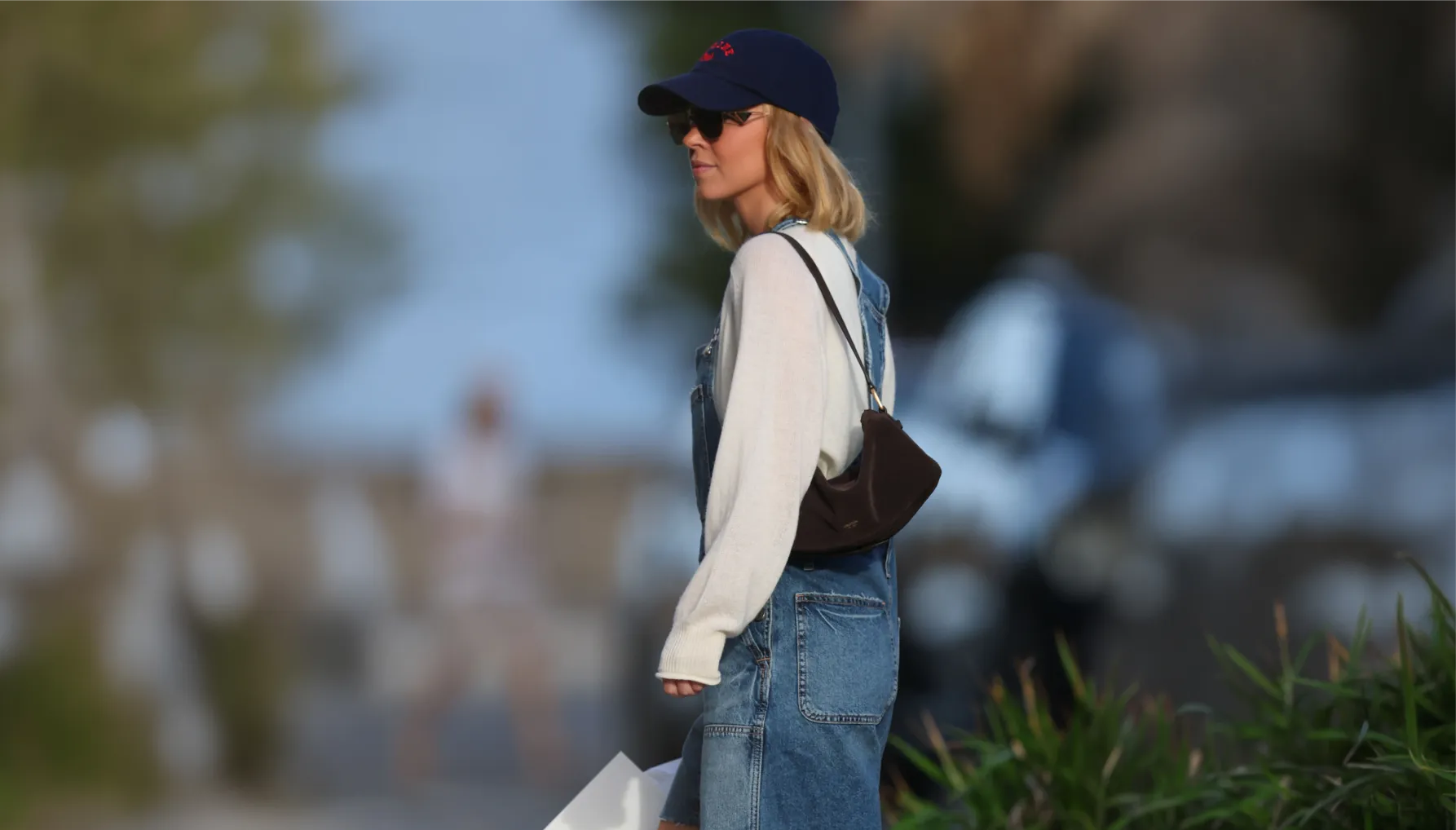 Person wearing a cap and overalls, standing outdoors with a blurred background.