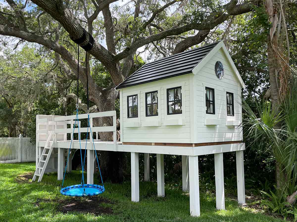 White and black custom playhouse with round top window on stilt in garden by WholeWoodPlayhouses