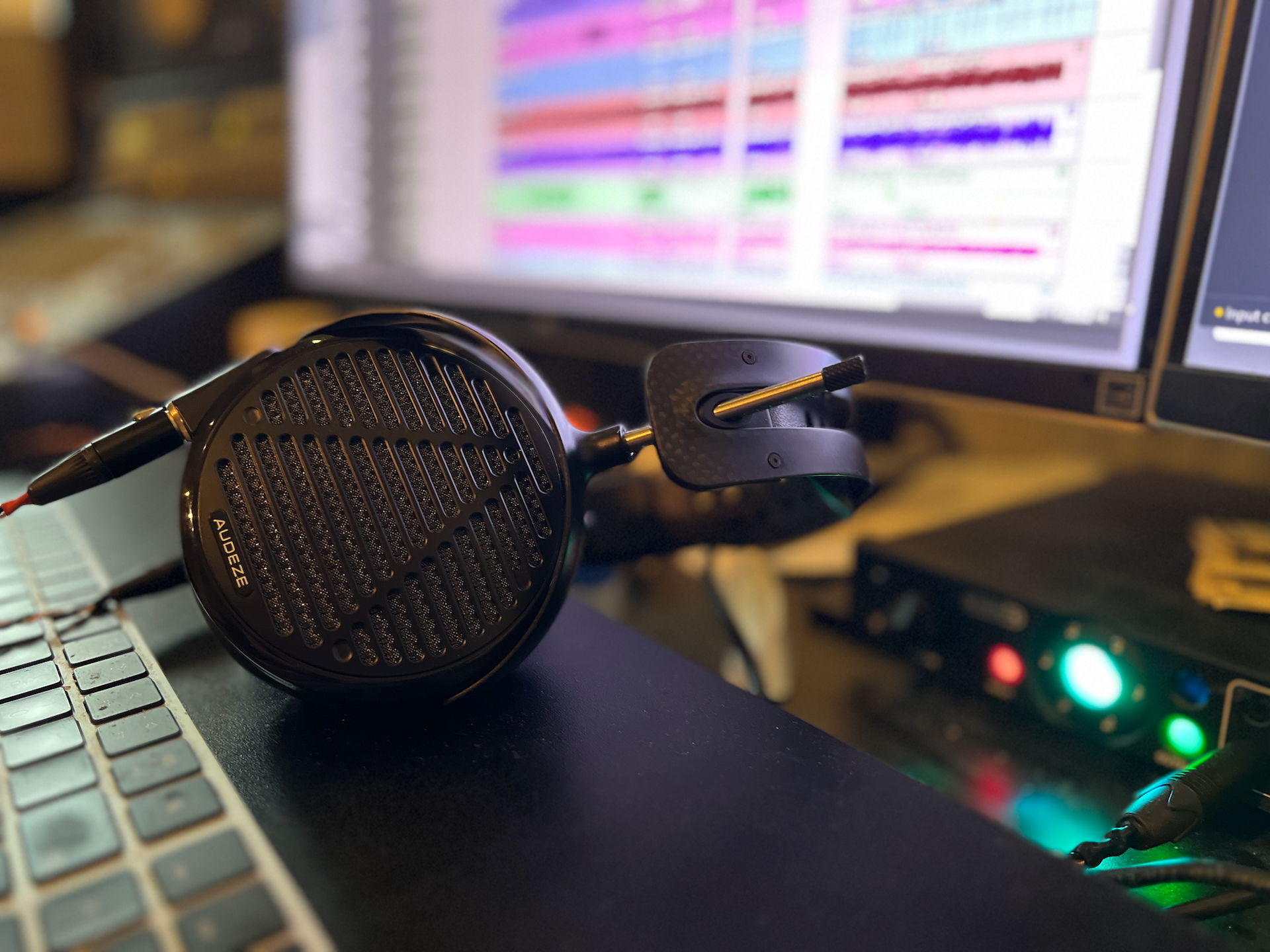 Audeze LCD-5 headphones resting on a laptop next to a computer screen displaying audio tracks.