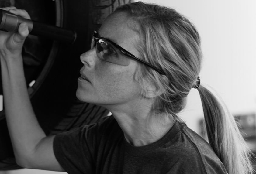 Woman inspecting a vehicle with a flashlight, wearing glasses.