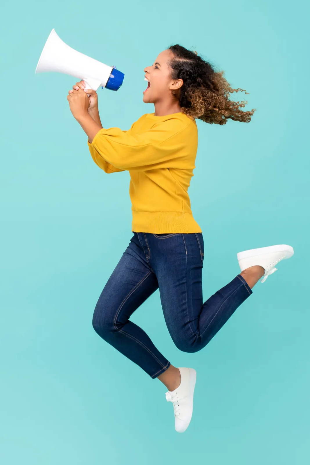Woman in shouting gleefully into megaphone while jumping into the air.