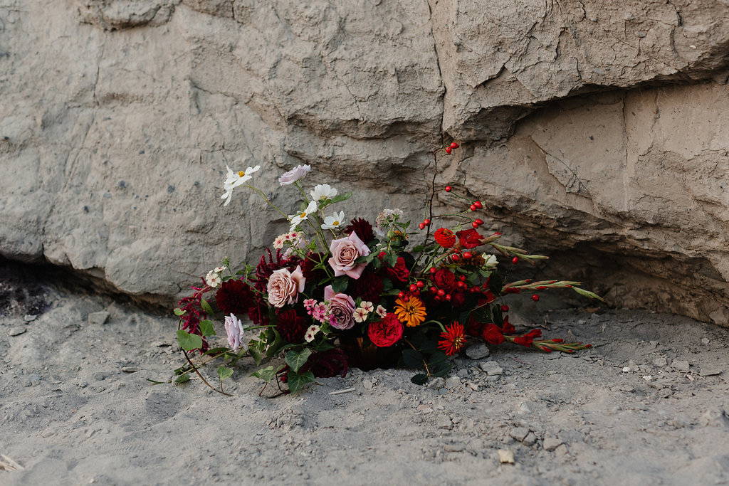 floral arrangement with red pink and yellow florals on the sand with cliff background