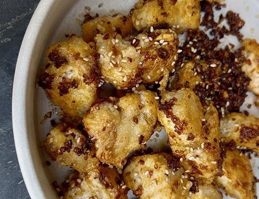 Bowl of crispy fried cauliflower pieces with sesame and spices.