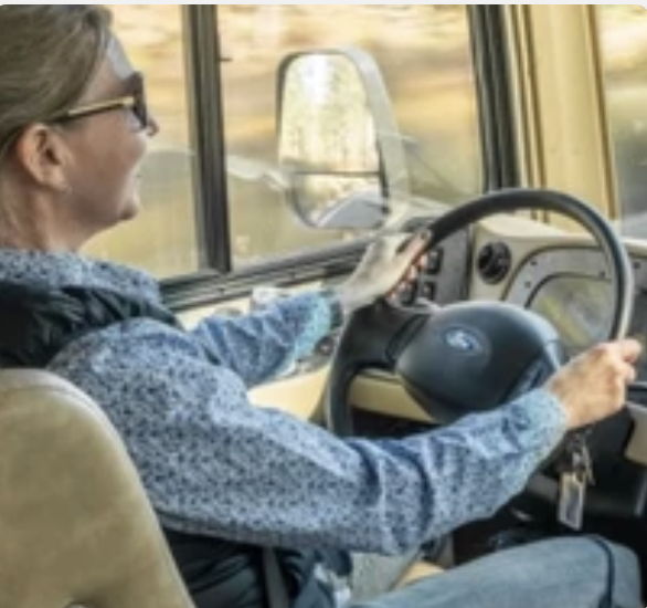 Person driving a vehicle, smiling, with hands on the steering wheel.