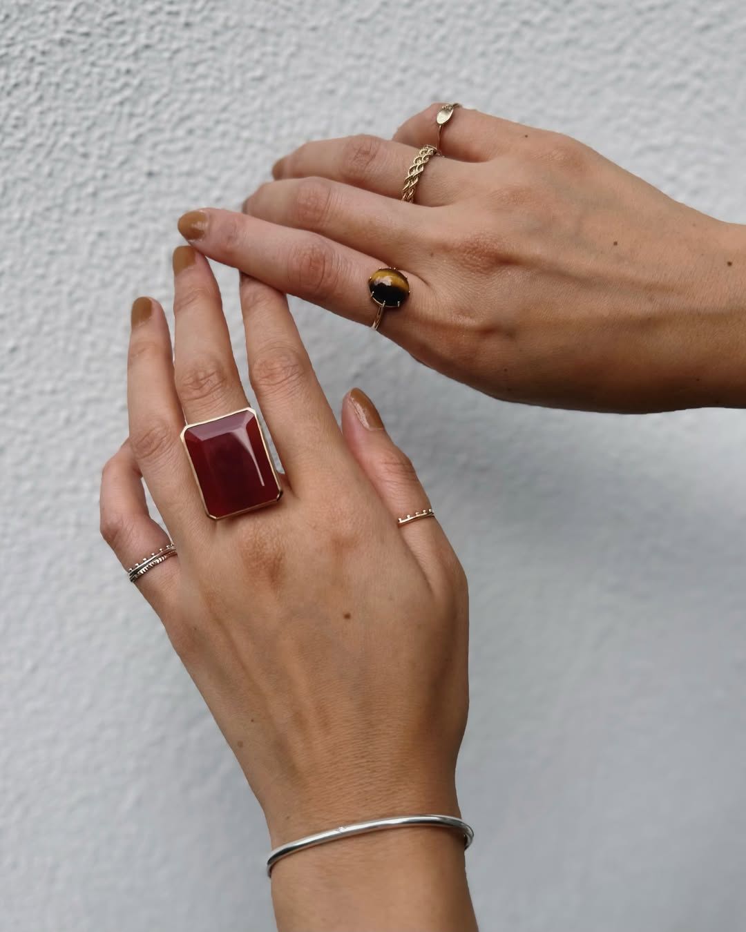 ジュエリー 重ね付け コーディネート Two hands wearing various rings, featuring a large red stone ring.