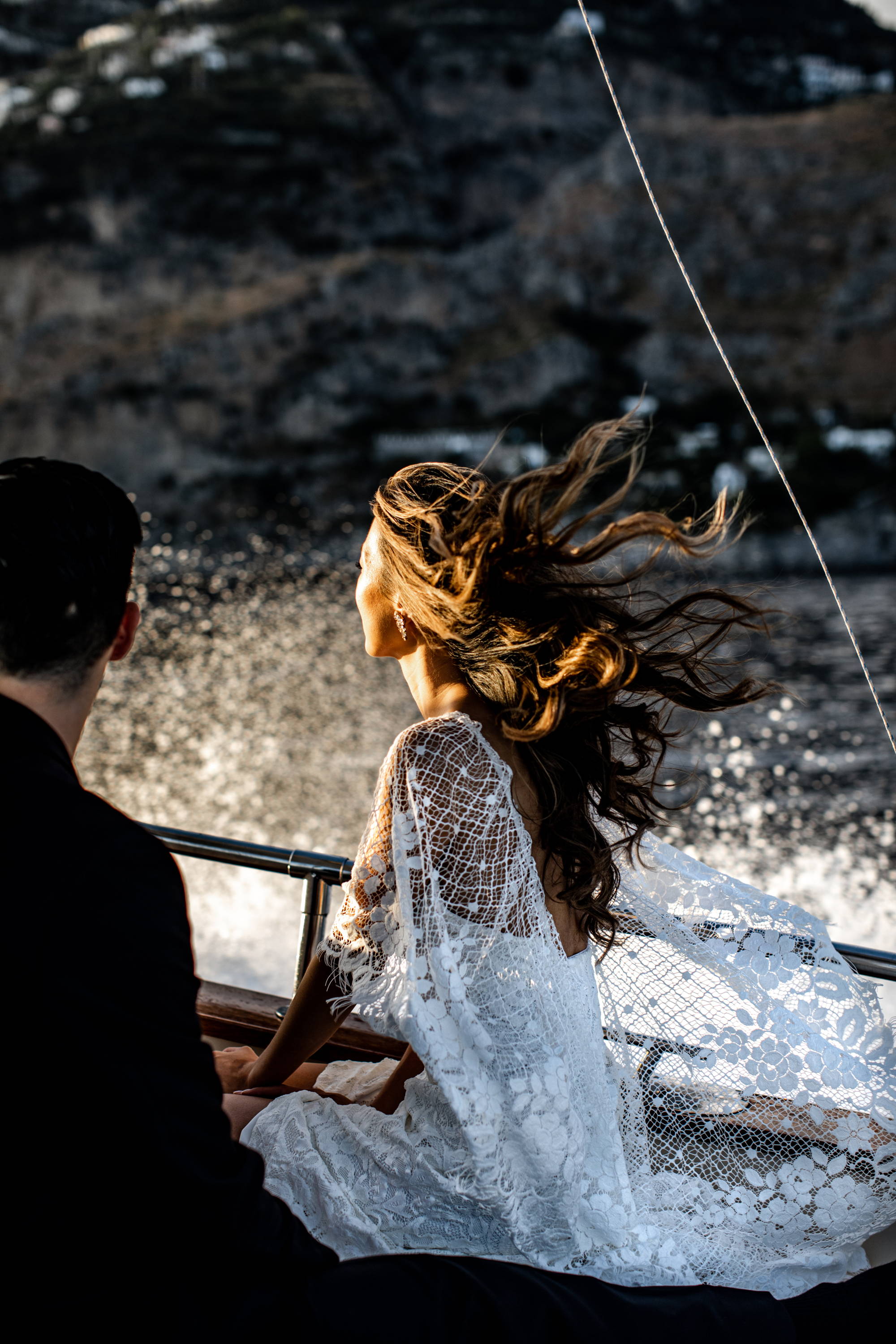 Mariée portant une robe de style cape en dentelle sur un bateau avec le vent soufflant sur ses cheveux. 