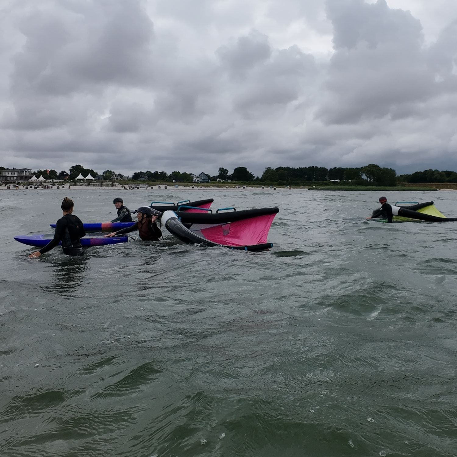 People wingfoiling in a cloudy body of water.