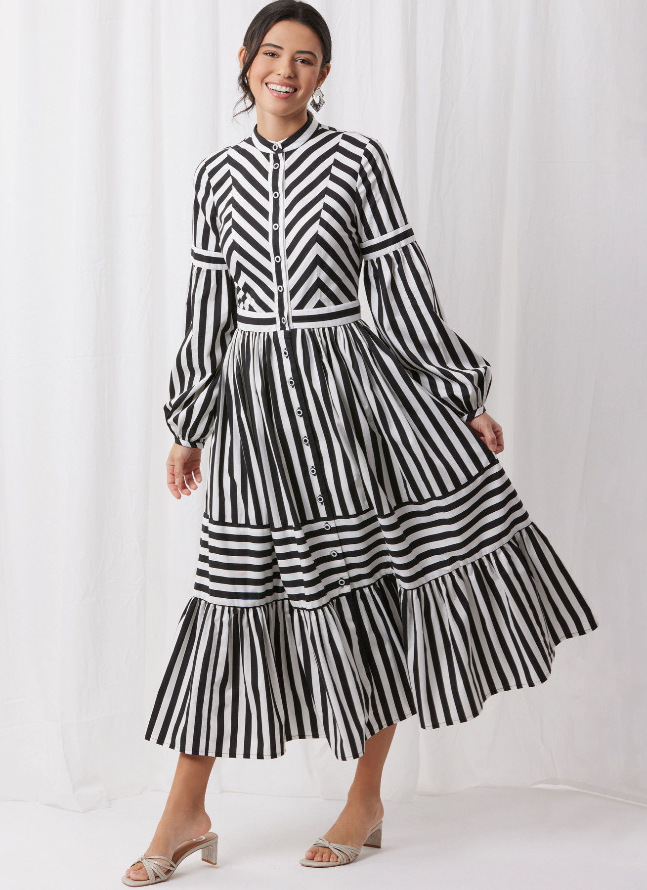 Woman in a black and white striped dress, smiling against a white background.