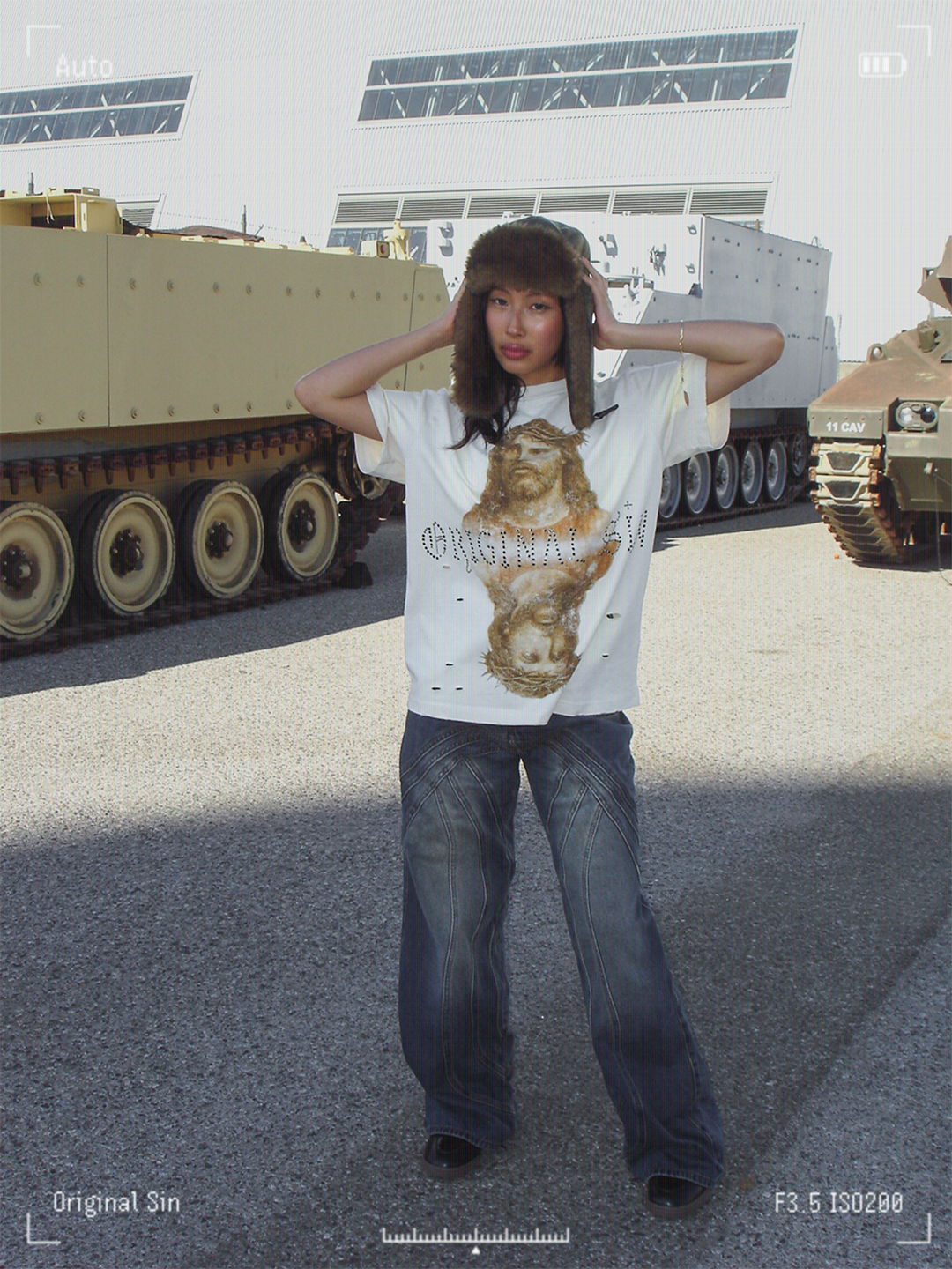 Person in casual outfit poses near military vehicles outdoors.