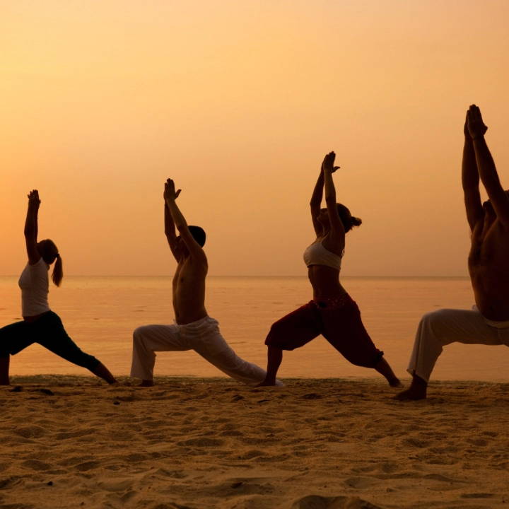 A group of people doing yoga on the beach during sunset