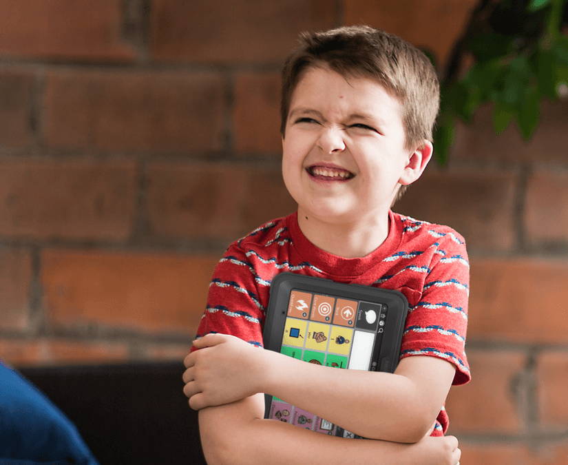 Young boy holding a Tobii Dynavox SC Tablet Mini in his arms.