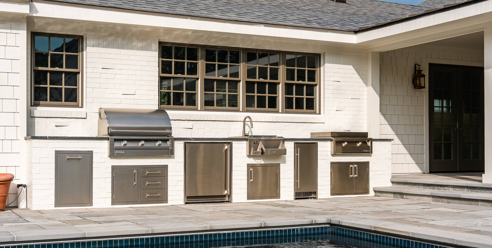 Outdoor kitchen area by a pool with modern appliances and a patio.
