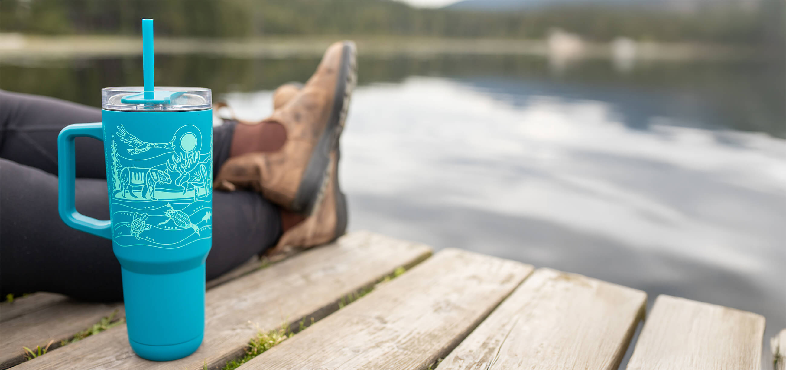 Teal 40oz insulated tumbler with straw on a dock by a mountain lake — Native Northwest Indigenous art drinkware