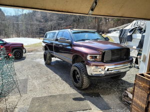 Lifted maroon Dodge Ram 1500 parked in a driveway with black wheels and camper shell