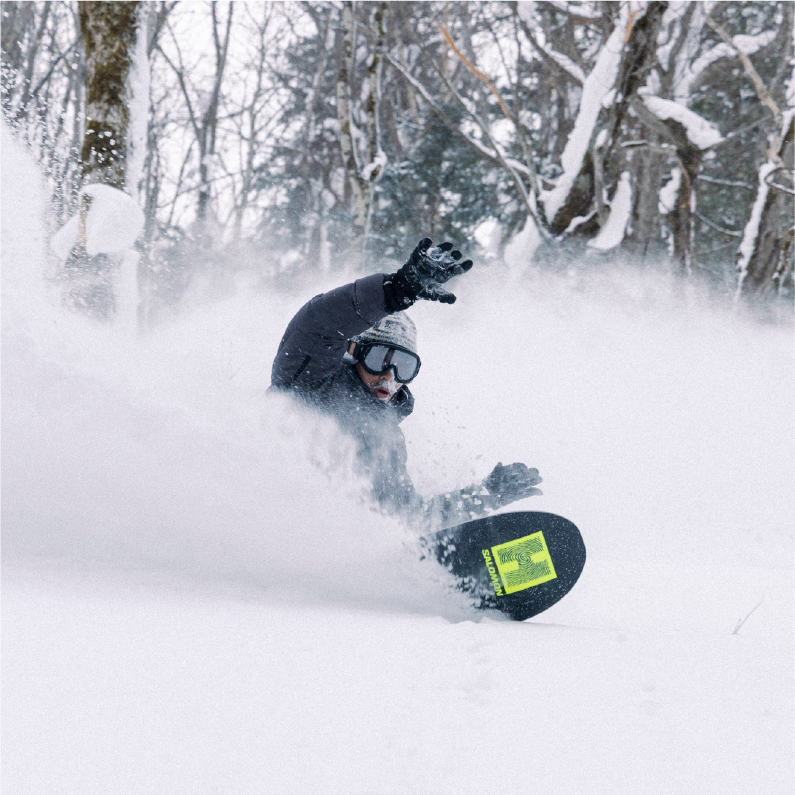 Person snowboarding through deep snow in a forest.