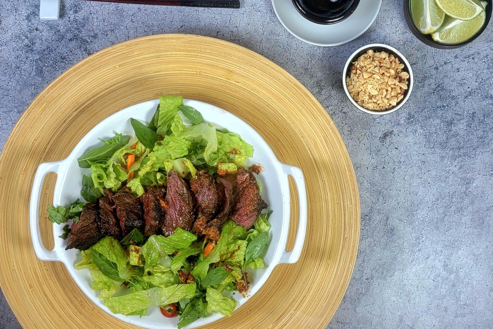 A bowl of salad with grilled meat, peanuts, lime, and sauces.