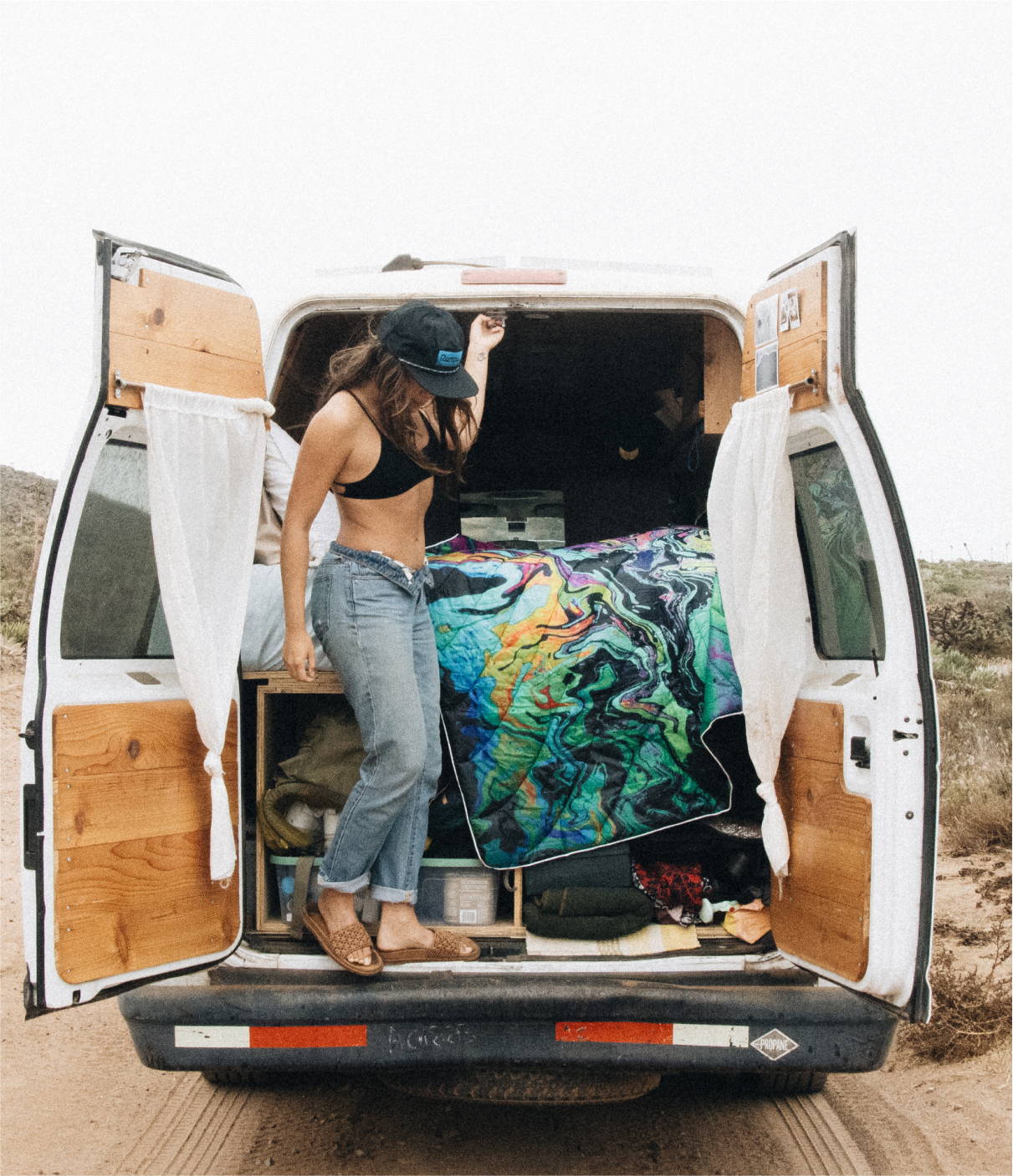 A woman stands in the back of a van with her Rumpl blanket, ready for a journey.