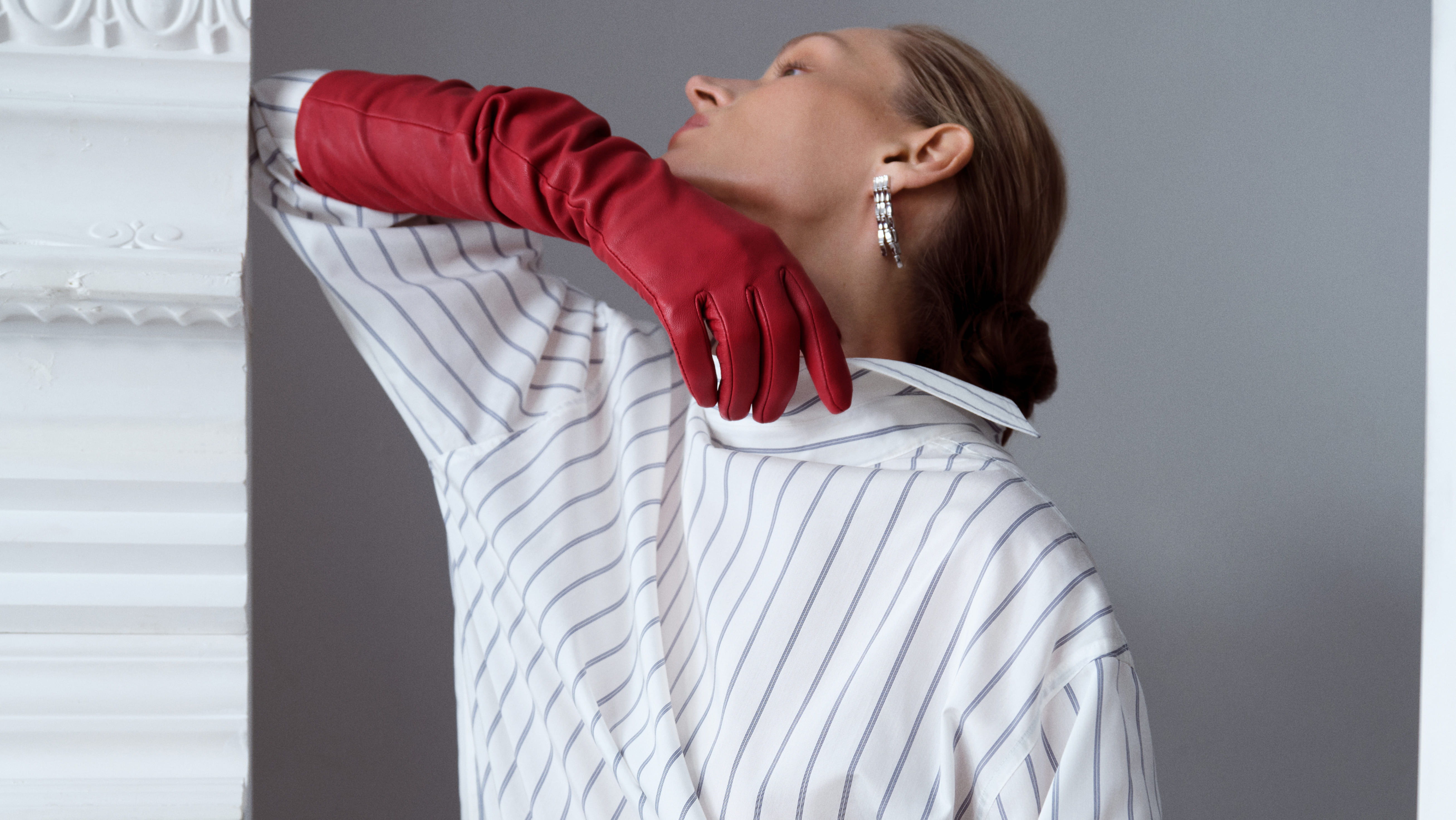 Model in striped outfit with red gloves posing against a gray background.