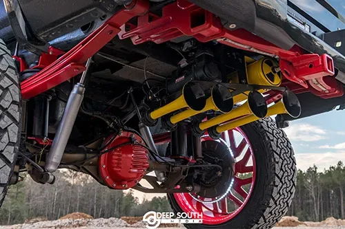 Lifted truck undercarriage with yellow train horns and red-painted suspension