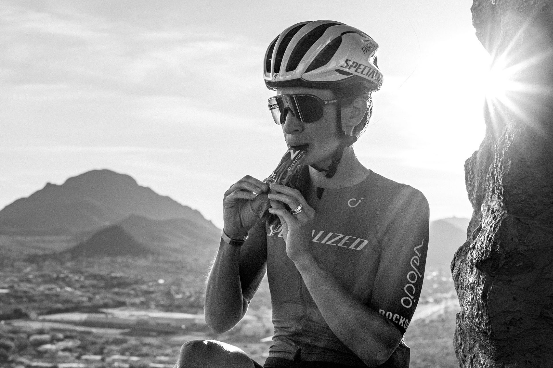 Eine Frau mit Fahrradhelm nimmt bei einer Pause auf einem Berg ein Gel von Neversecond zu sich.
