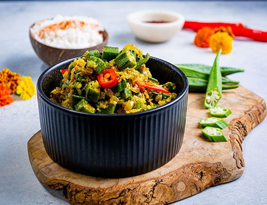 Bowl of vegetable curry with rice, spices, and garnishes on a wooden board.