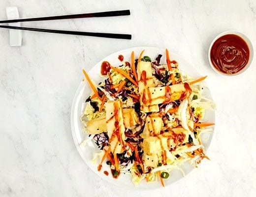 A plate of salad with grilled chicken, carrots, and dipping sauce.