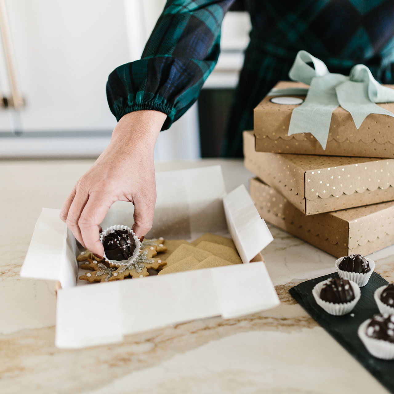 Person placing a chocolate treat into a gift box surrounded by baked goods.