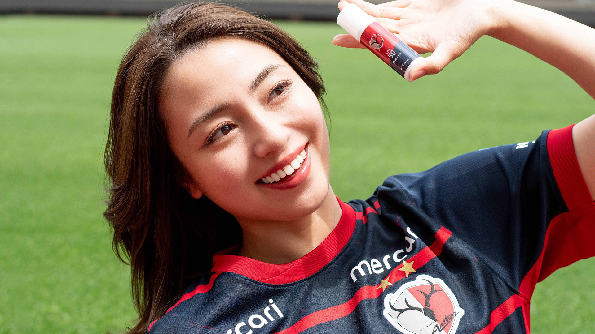 Smiling woman in sports jersey holding a product, outdoors.