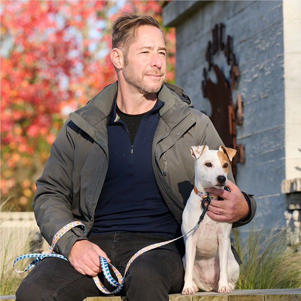 Man sitting with a small dog on a leash in a park.