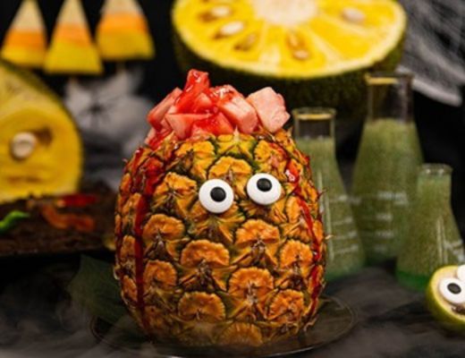 Pineapple with eyes and toppings, surrounded by other fruit and decorations.