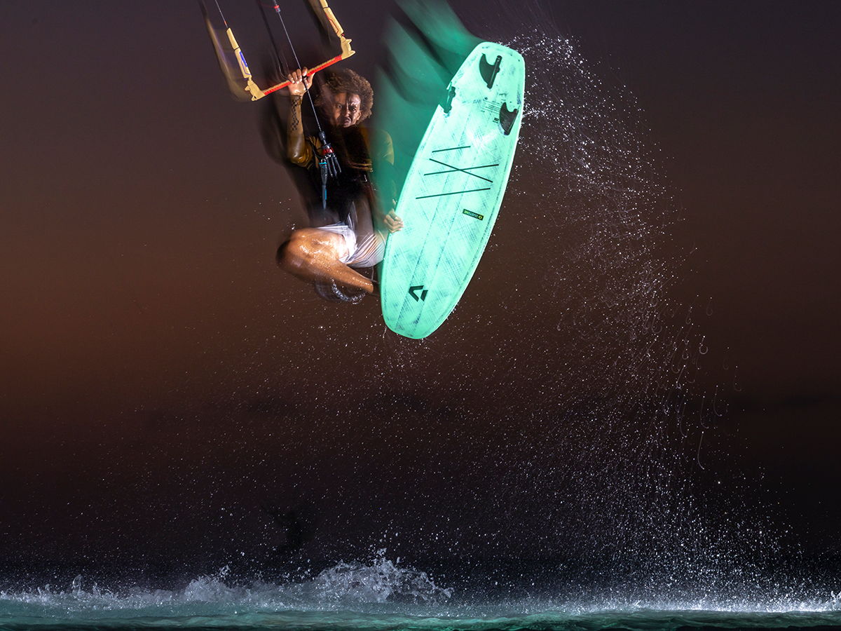 Kiteboarder performing a jump over water at sunset.