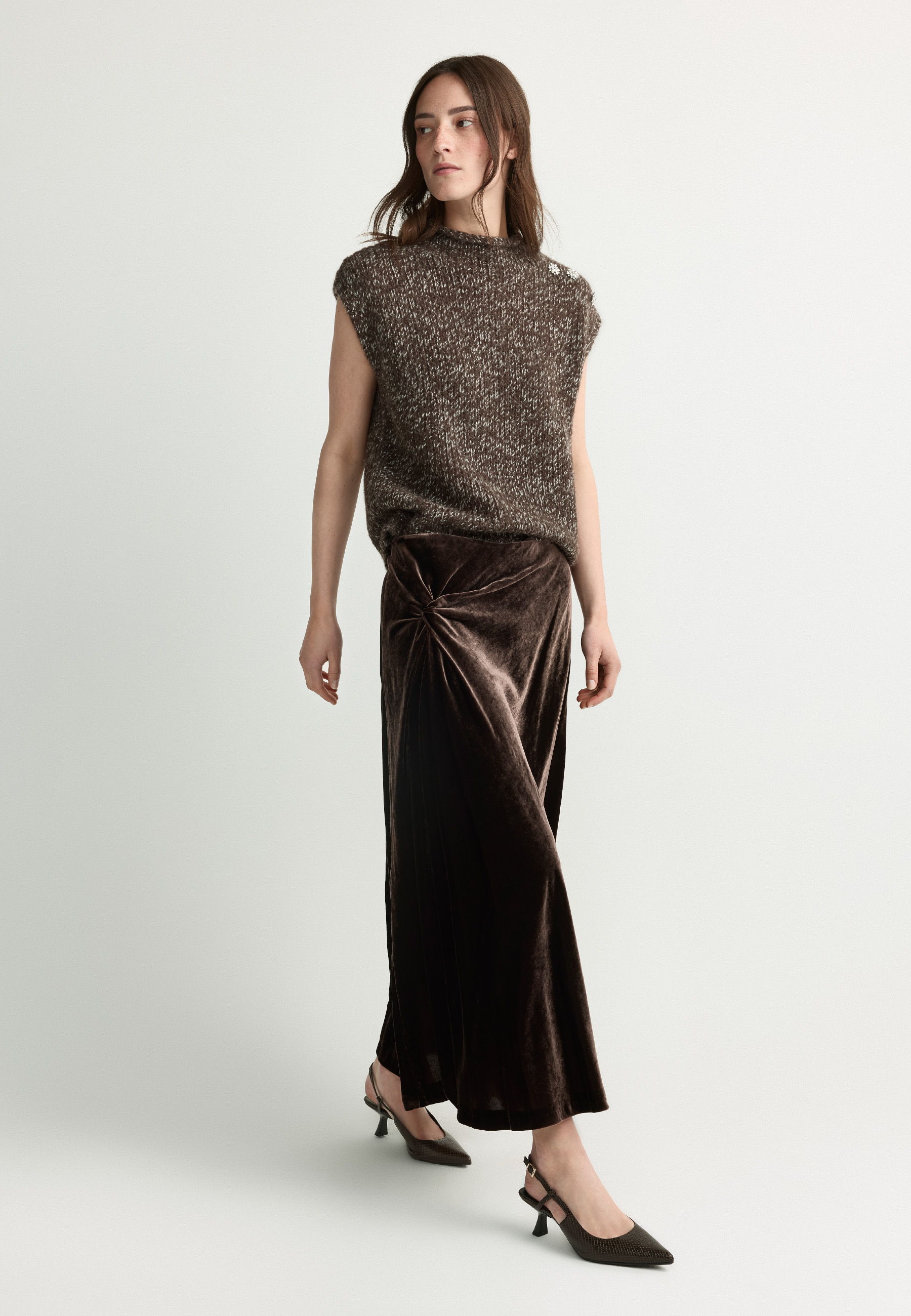 A woman in a stylish outfit poses in a minimalist setting.