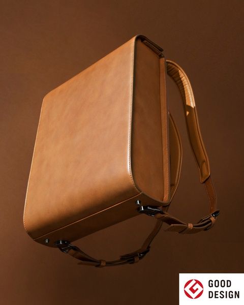 A stylish brown leather bag with a shoulder strap against a brown background.