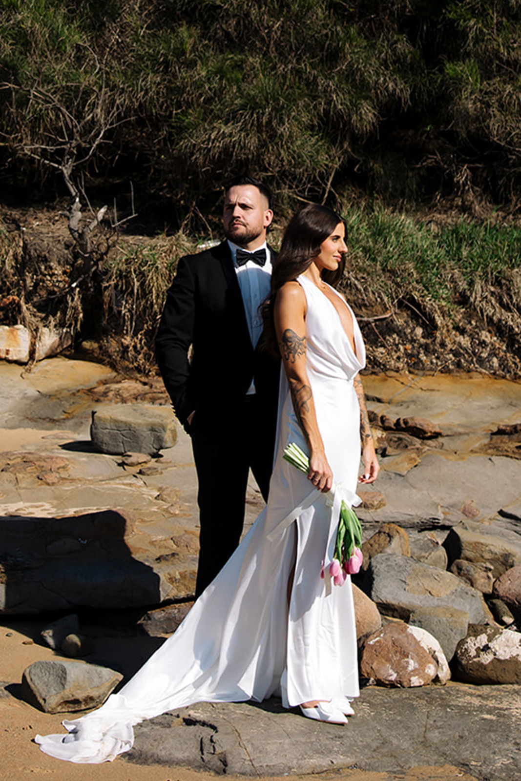 Bride and groom standing on rocks, wearing formal wedding attire.