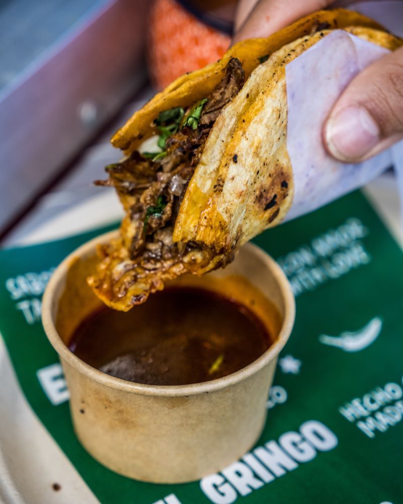 A hand holding a taco above a cup of sauce.