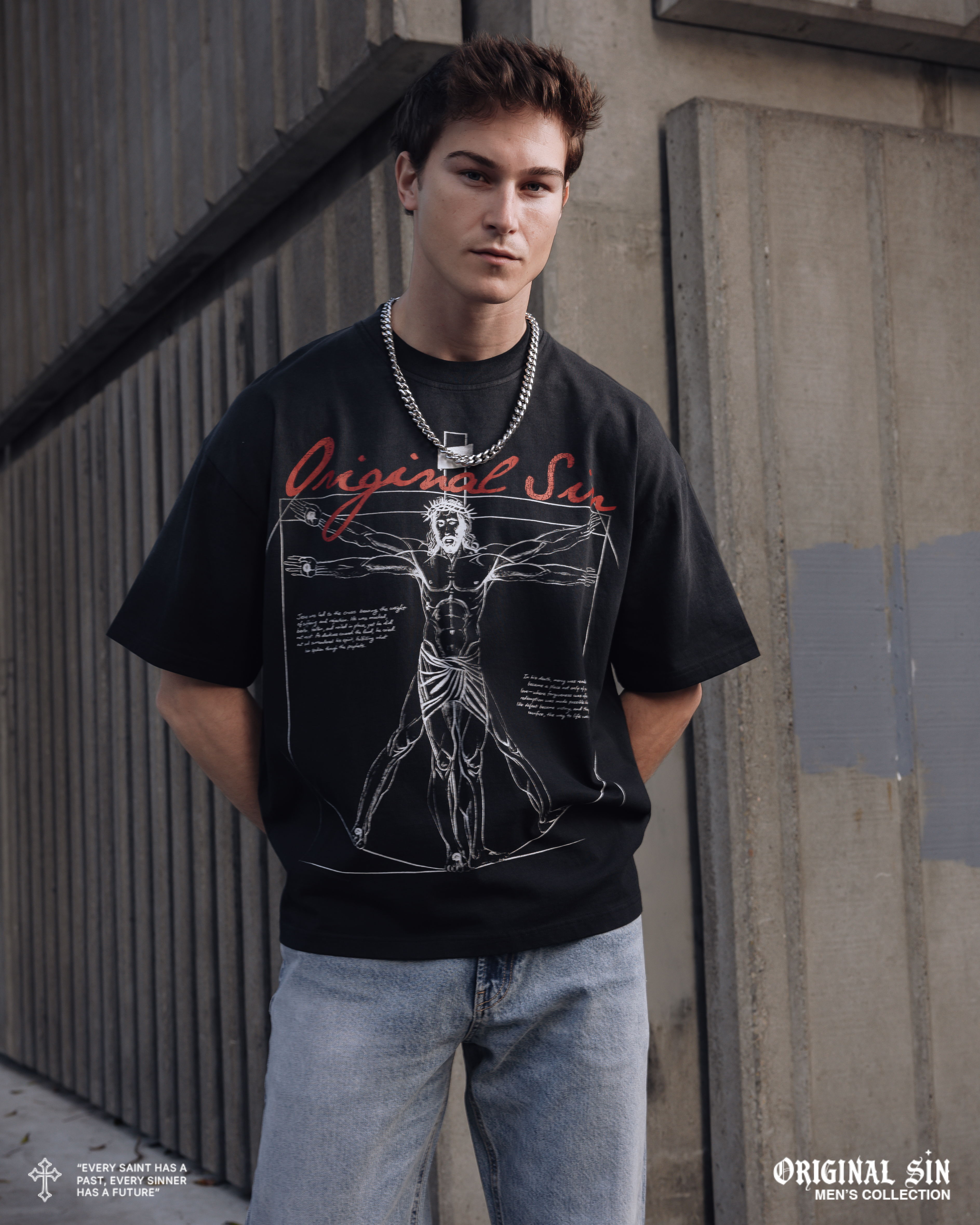 Young man in a graphic t-shirt standing against a wall.