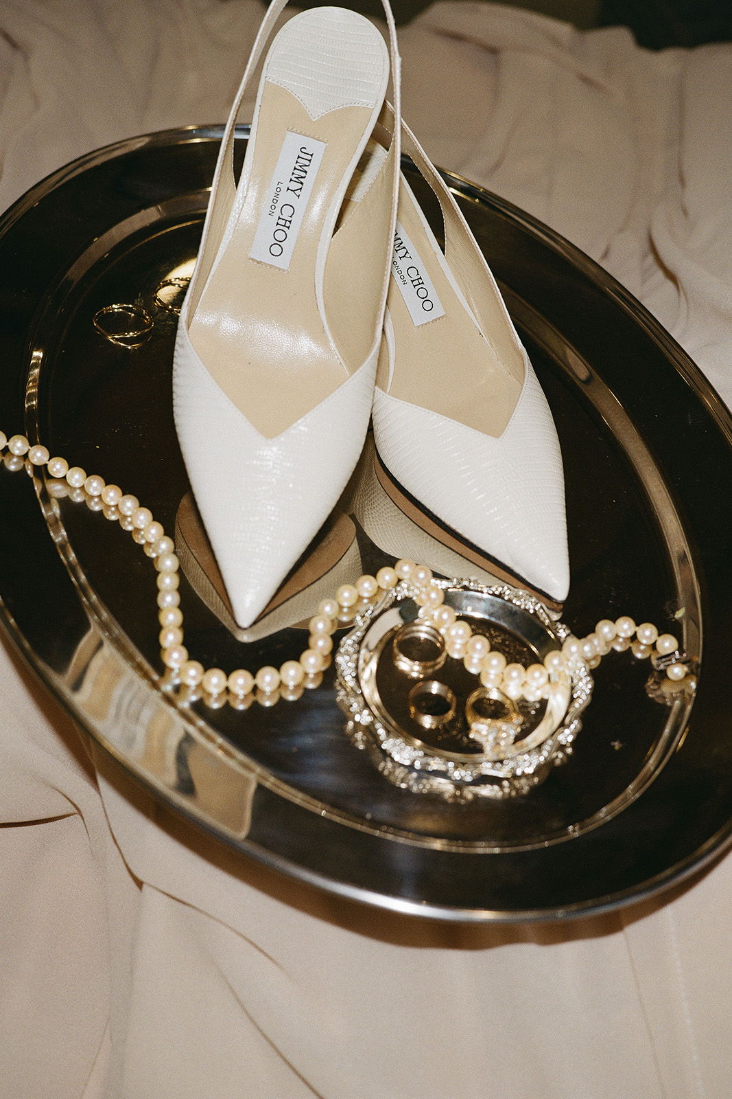 White heels and jewelry on a silver tray.
